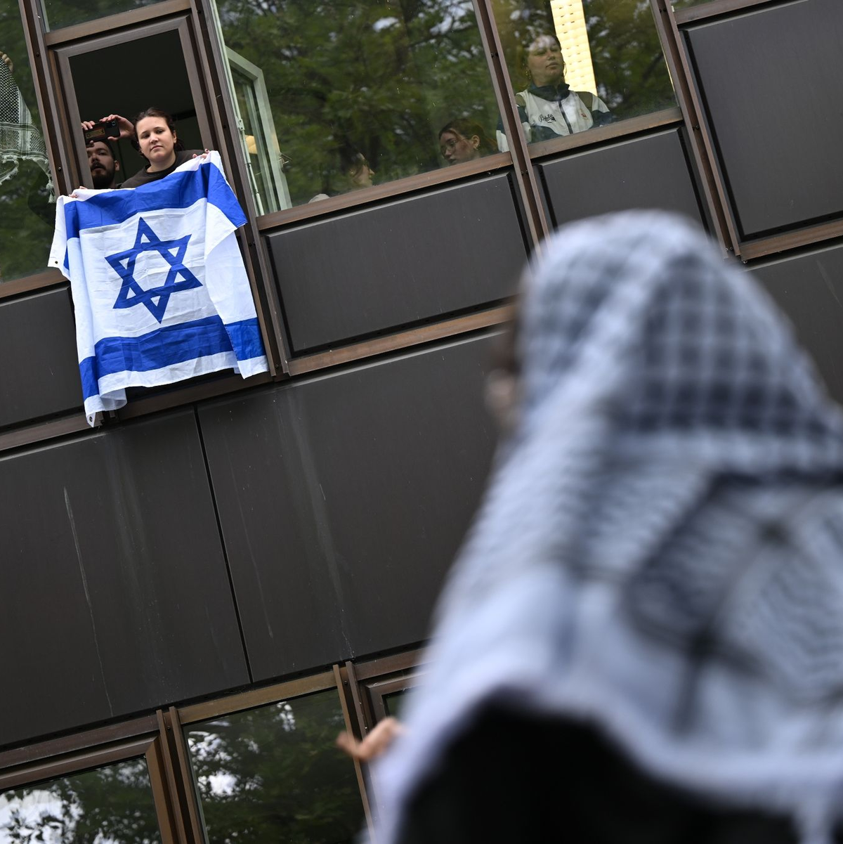 Eine Frau hält eine Israelflagge aus dem Fenster: Die propalästinensische Demonstration auf dem Theaterhof der Freien Universität Berlin wird von Polizisten beobachtet. - Foto: Sebastian Christoph Gollnow/dpa