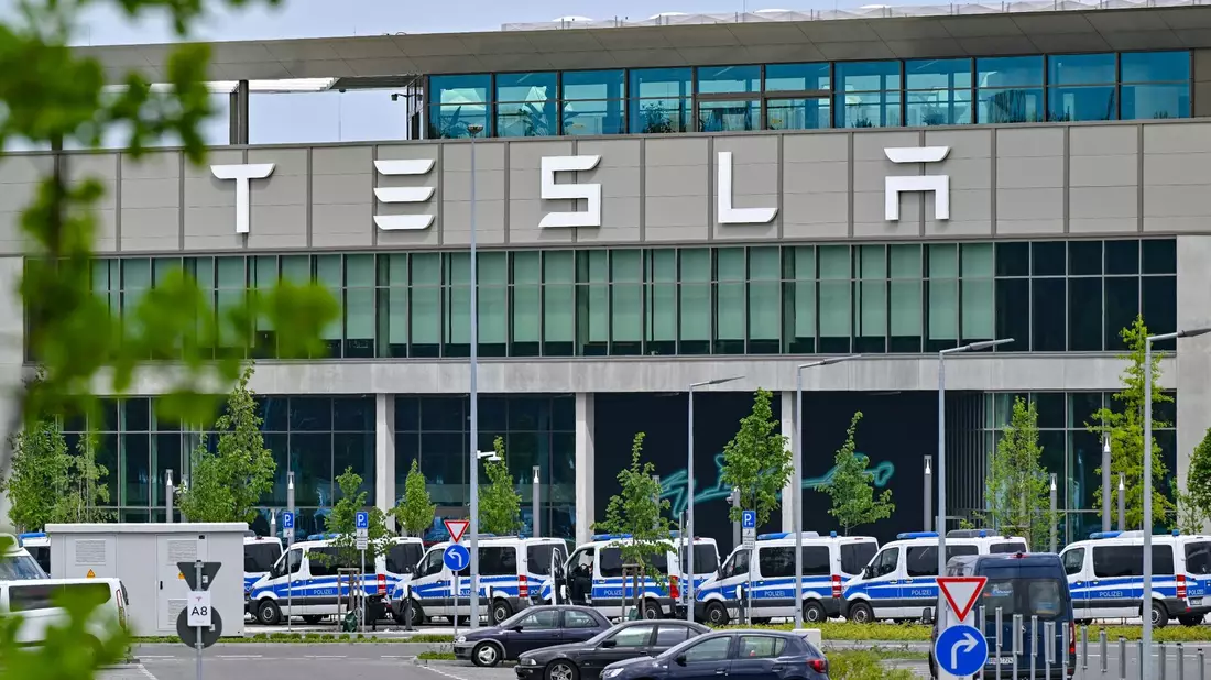 Polizeifahrzeuge stehen am Samstagvormittag vor dem Haupteingang des Tesla-Werks in Grünheide. - Bild: Patrick Pleul/dpa