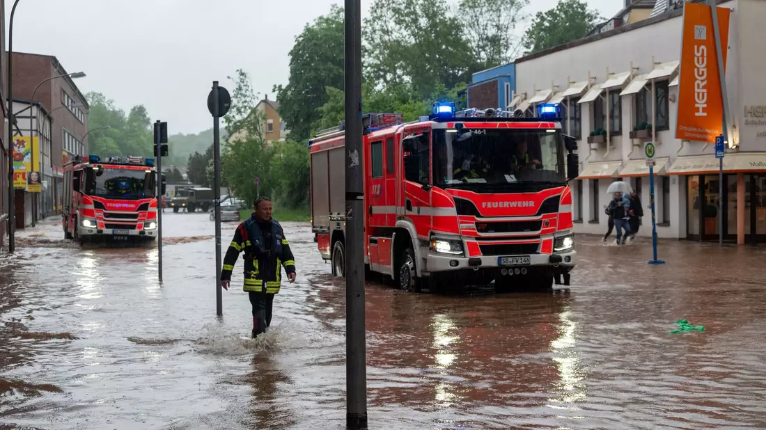 Feuerwehrleute bewegen sich durch das Hochwasser in Saarbrücken. - Bild: Harald Tittel/dpa