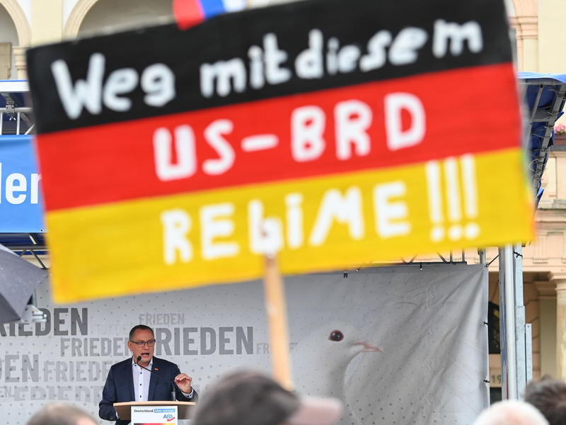 Ein antiamerikanisches Plakat auf einer AfD-Kundgebung mit Bundessprecher Tino Chrupalla in Magdeburg (Archivbild). - Foto: Heiko Rebsch/dpa