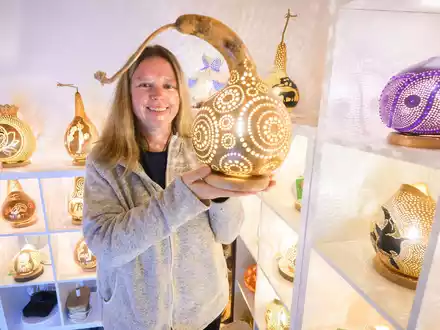Virginia Lauterbach präsentiert eine ihrer handgefertigten Kürbislampen in der Kalebassenmanufaktur in Bückeburg. - Foto: Julian Stratenschulte/dpa