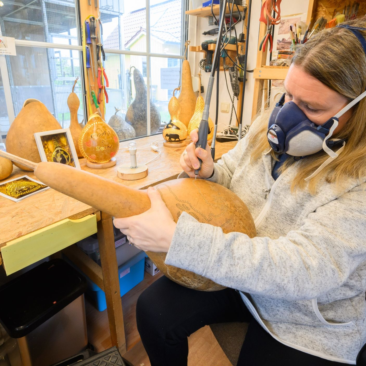 Virginia Lauterbach bearbeitet in ihrer Werkstatt einen Flaschenkürbis mit einem Bohrer. - Foto: Julian Stratenschulte/dpa