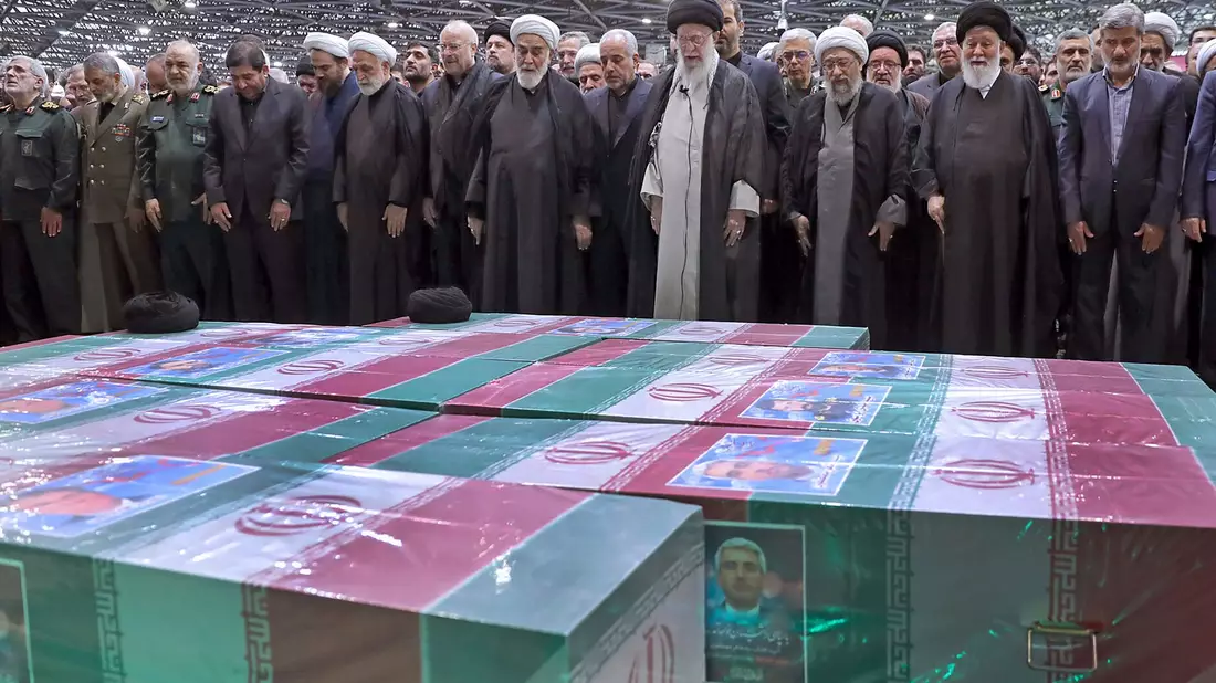 Abschied von Präsident Ebrahim Raisi, Außenminister Hussein Amirabdollahian und den weiteren beim Hubschrauberabsturz Getöteten: Irans Religionsführer Ajatollah Ali Chamenei (M.r.) spricht in Teheran an den mit Flaggen bedeckten Särgen ein Gebet. - Bild: Uncredited/Office of the Iranian Supreme Leader/AP/dpa