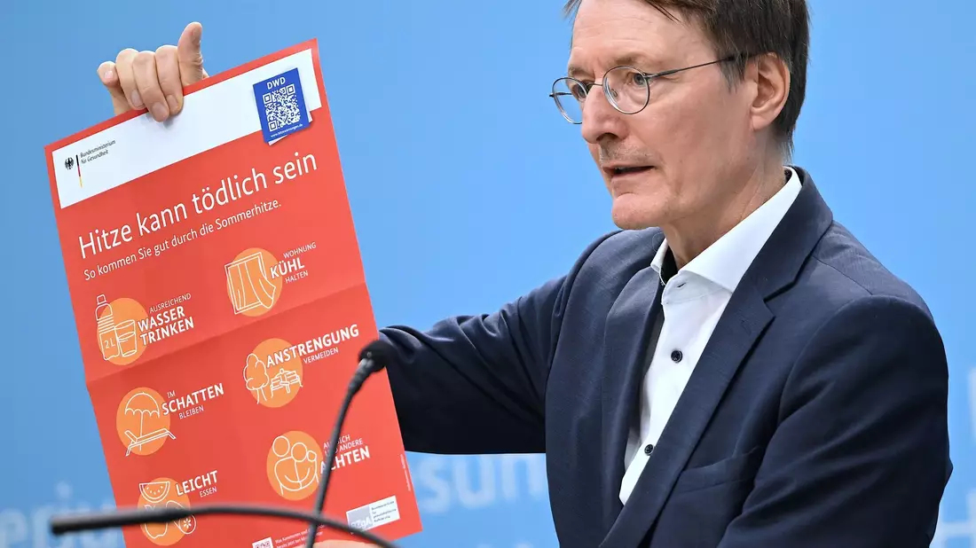 Bundesgesundheitsminister Karl Lauterbach (SPD) hält ein Plakat zum Thema Hitzeschutz hoch. - Bild: Britta Pedersen/dpa