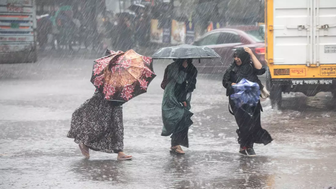 Frauen gehen bei Regen über eine Straße in Bangladesch. - Bild: Md. Rakibul Hasan/ZUMA Press Wire/dpa