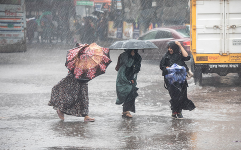 Frauen gehen bei Regen über eine Straße in Bangladesch. - Foto: Md. Rakibul Hasan/ZUMA Press Wire/dpa