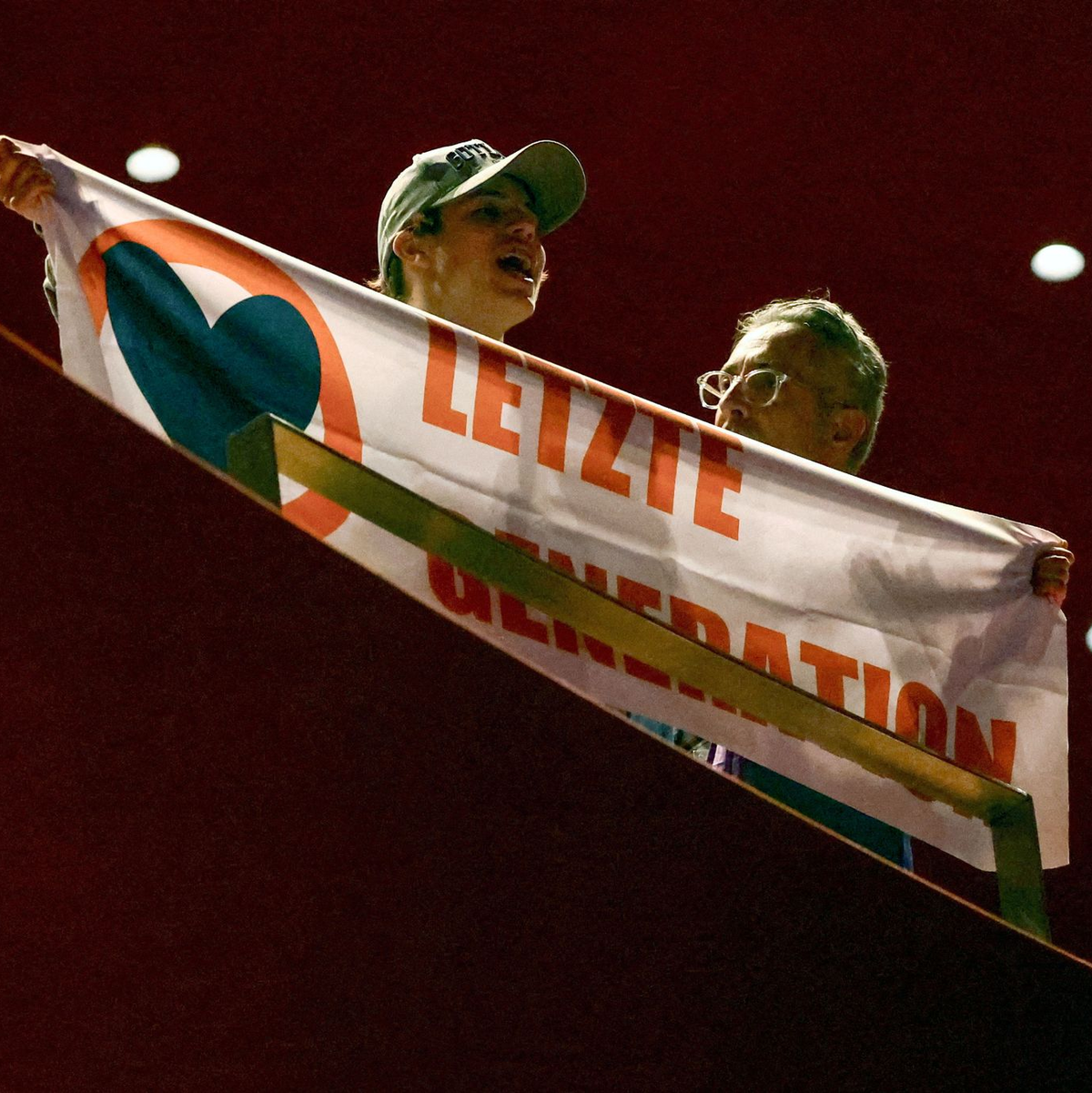 Ein Aktivist der Letzten Generation zeigt während der Podiusmdiskussion mit Kanzler Scholz ein Transparent. - Foto: Kai Pfaffenbach/REUTERS POOL/dpa