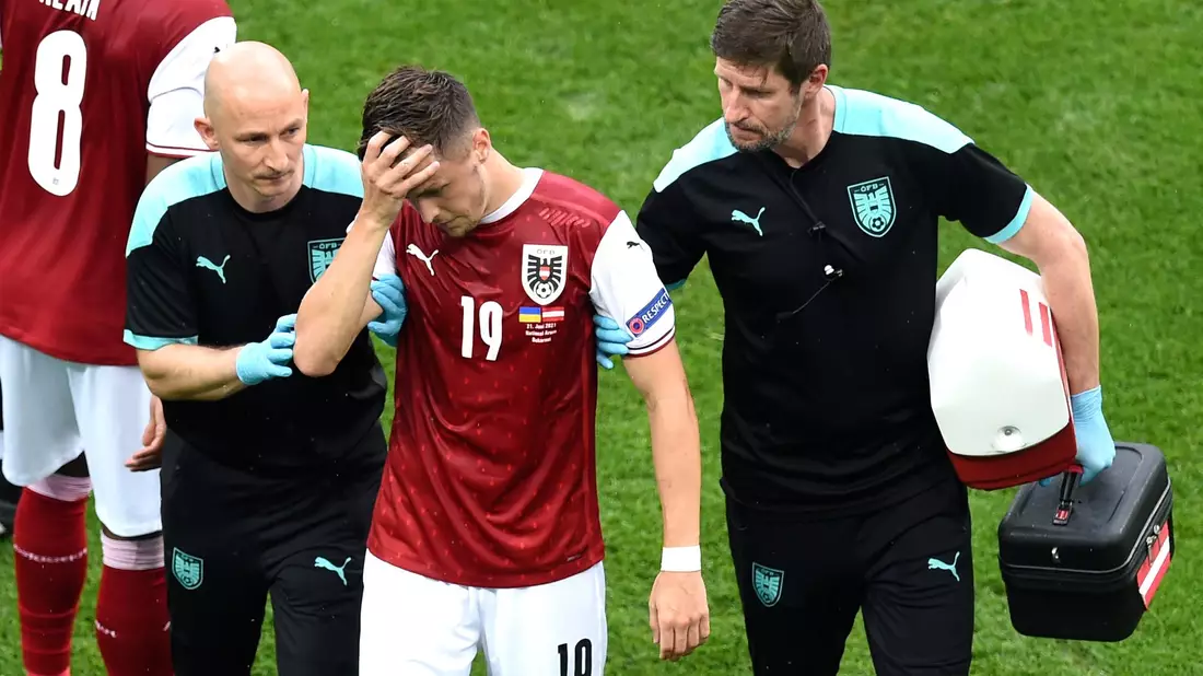 Christoph Baumgartner (M) aus Österreich wird nach einer Verletzung von medizinischen Mitarbeitern vom Spielfeld geführt. - Bild: Mihai Barbu/Pool AFP/AP/dpa