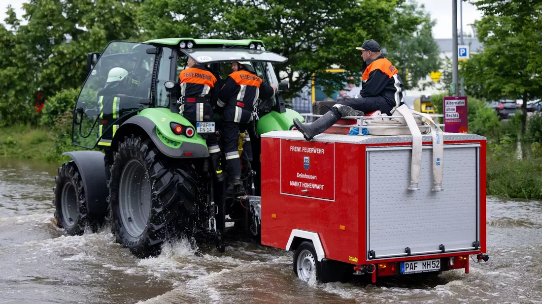 Feuerwehrleute fahren in Reichertshofen über eine überflutete Straße. - Bild: Sven Hoppe/dpa