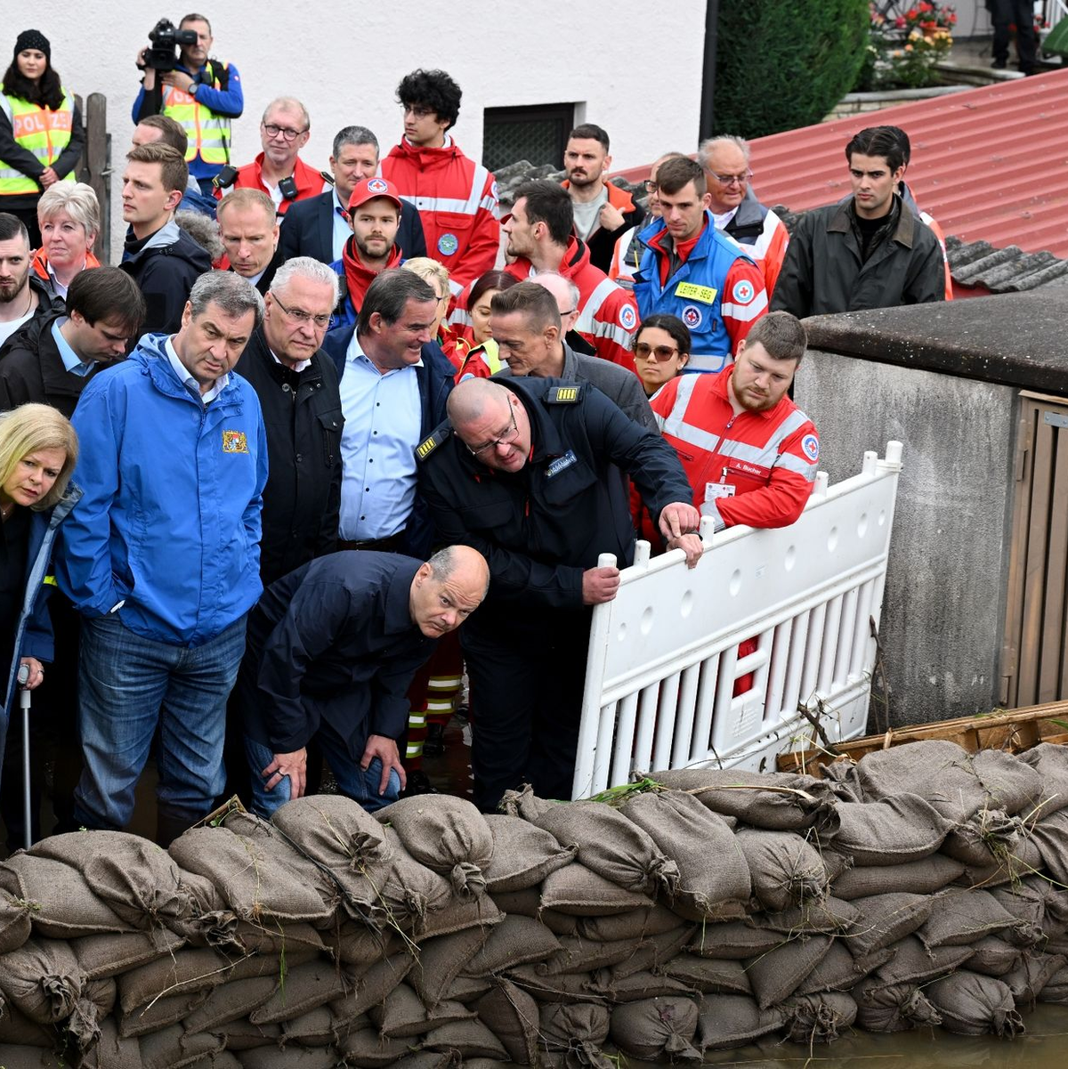 Bundeskanzler Olaf Scholz (1. Reihe, v.r.), Bayerns Innenminister Joachim Herrmann, Ministerpräsident Markus Söder und Bundesinnenministerin Nancy Faeser stehen hinter einer Absperrung aus gefüllten Sandsäcken bei einer Ortsbesichtigung in Reichertshofen. - Foto: Sven Hoppe/dpa