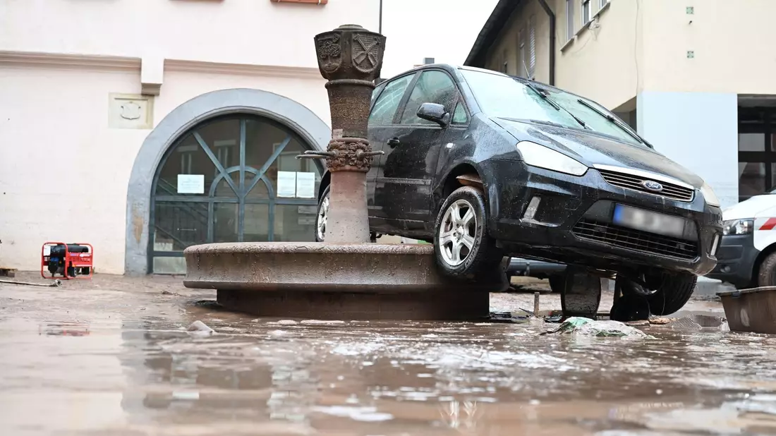 Auf einem Brunnen in Rudersberg hängt ein durch das Hochwasser weggespültes Auto. - Bild: dpa