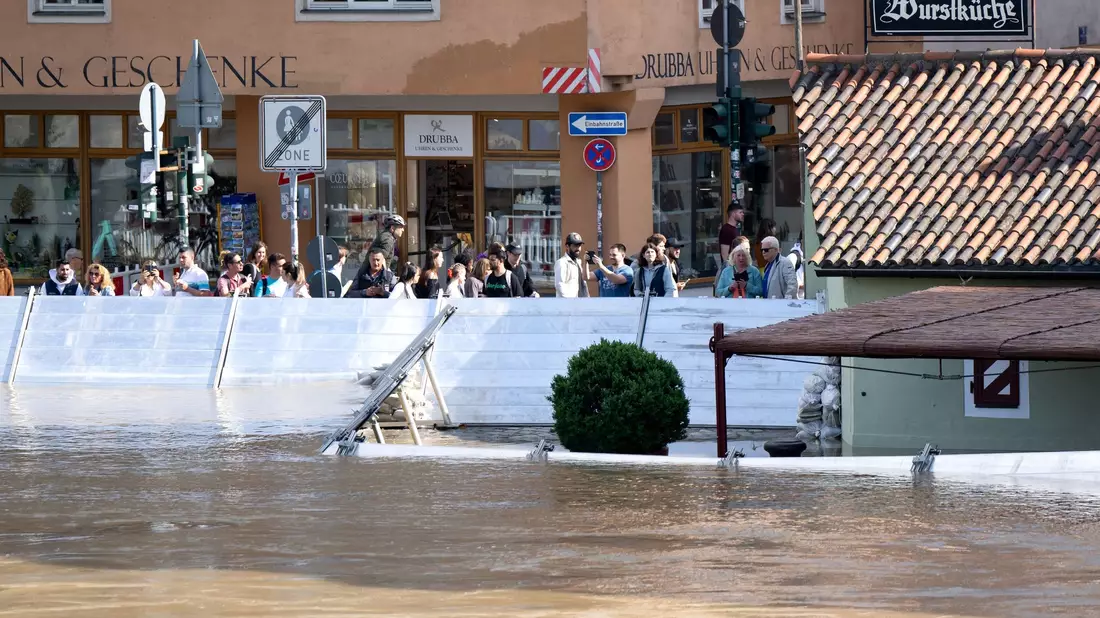 Menschen schauen sich in der Altstadt von Regensburg hinter einer Schutzwand das Hochwasser an. - Bild: Sven Hoppe/dpa