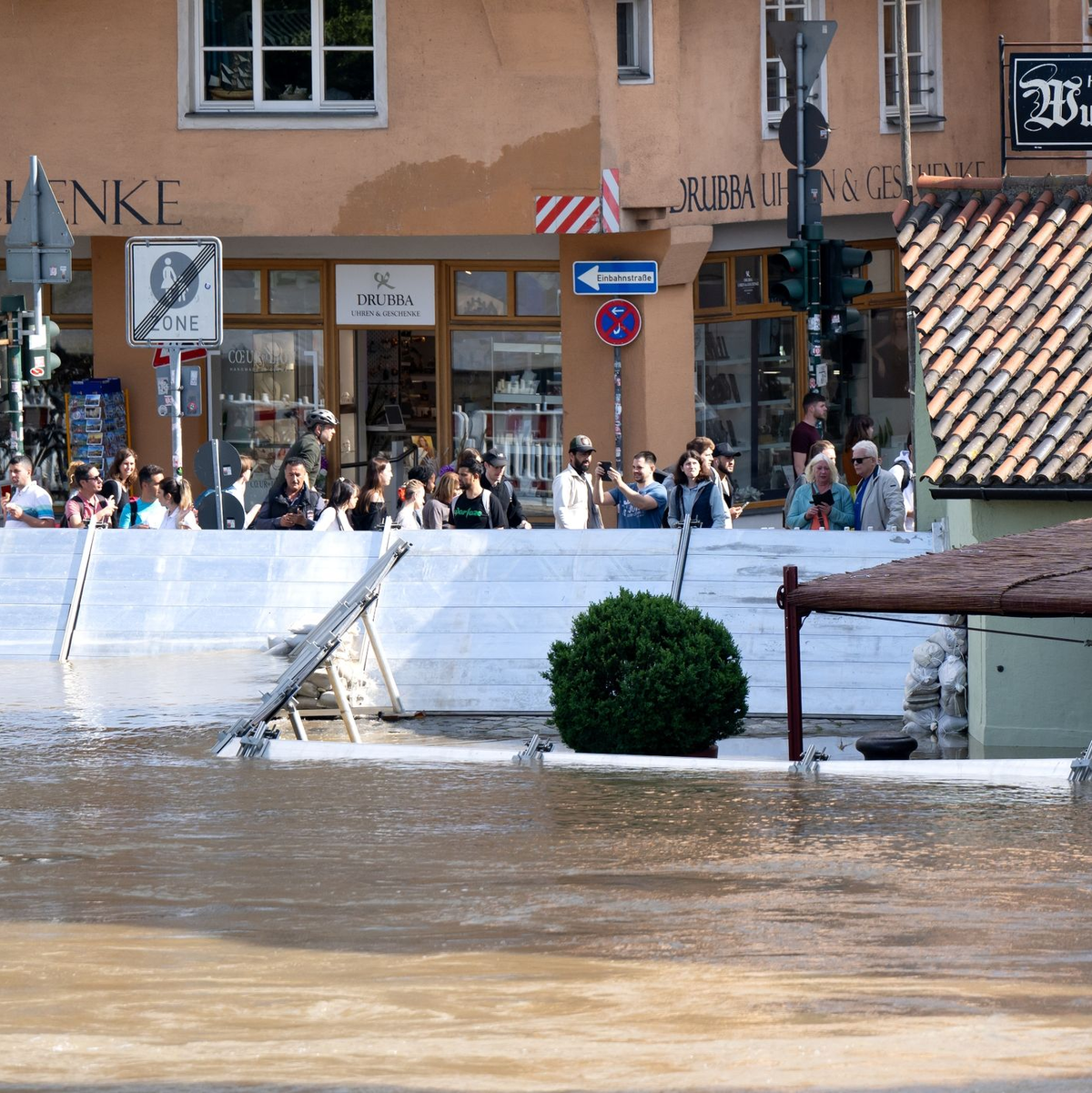 Menschen schauen sich in der Altstadt von Regensburg hinter einer Schutzwand das Hochwasser an. - Foto: Sven Hoppe/dpa