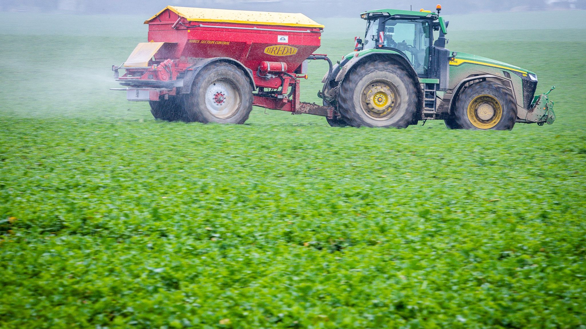 Ein Traktor fährt mit einem Streuwagen über ein Feld und bringt Dünger aus. - Foto: dpa