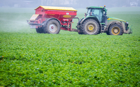 Ein Traktor fährt mit einem Streuwagen über ein Feld und bringt Dünger aus. - Foto: dpa