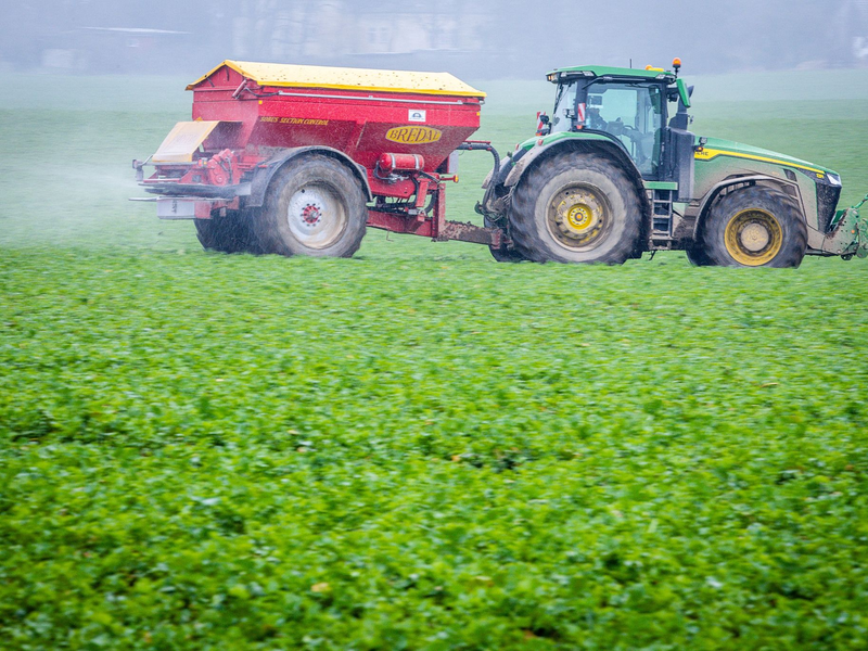 Ein Traktor fährt mit einem Streuwagen über ein Feld und bringt Dünger aus. - Foto: dpa