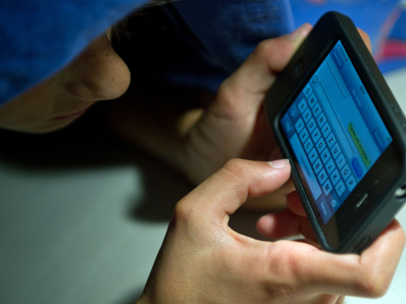 Ein elfjähriger Junge liegt unter der Bettdecke und schreibt auf einem Smartphone eine SMS. Kinder unter 13 Jahren sollten Experten zufolge keinen Zugang zu derartigen Medien haben. - Foto: Patrick Pleul/dpa