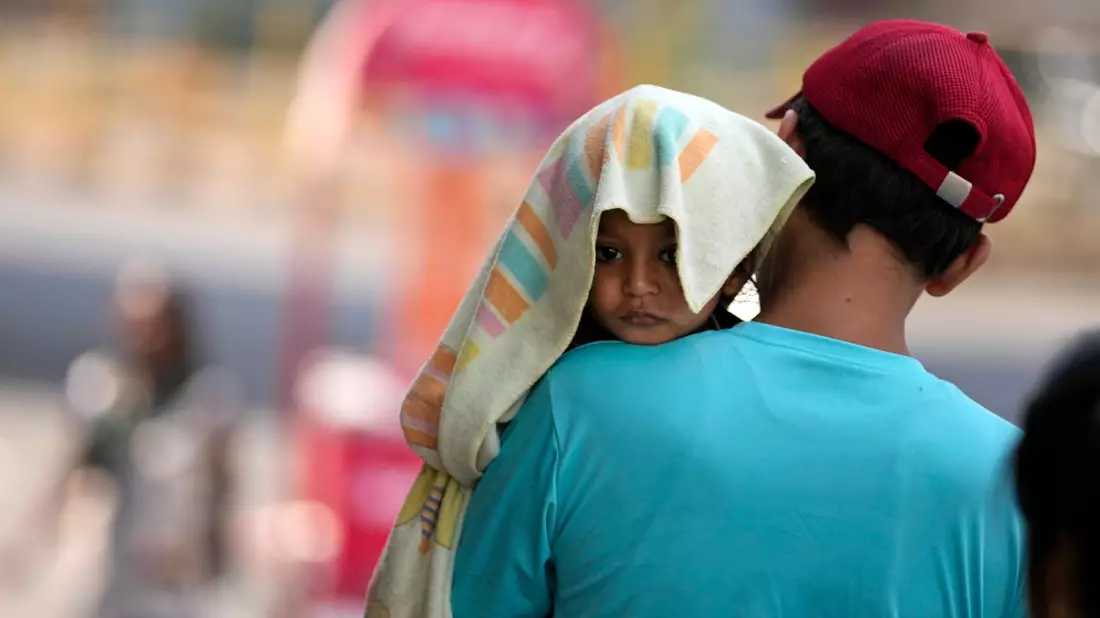 Ein Mann trägt ein Kind, dessen Kopf mit einem Handtuch bedeckt ist. - Bild: Channi Anand/AP/dpa