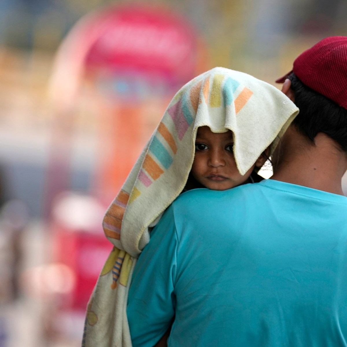 Ein Mann trägt ein Kind, dessen Kopf mit einem Handtuch bedeckt ist. - Foto: Channi Anand/AP/dpa