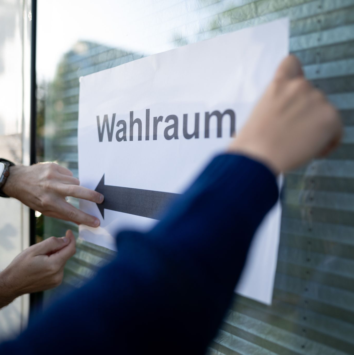 Wahlhelfer hängen einen Zettel, auf dem „Wahlraum“ steht, auf. - Foto: Fabian Strauch/dpa