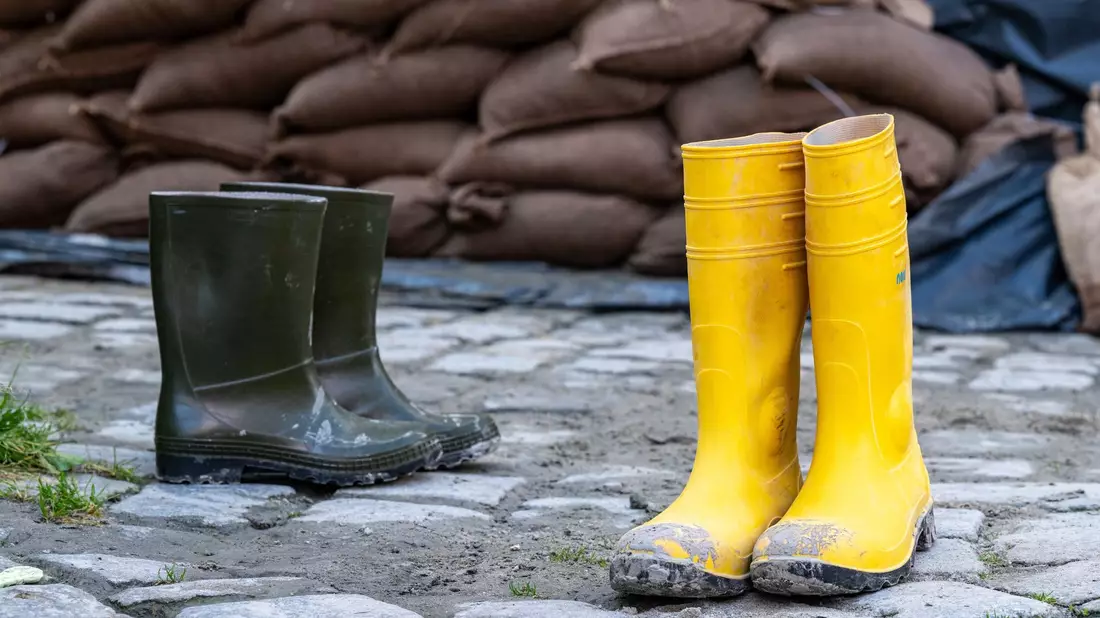 Gummistiefel stehen in der Altstadt vor Sandsäcken. Der Hochwassernachrichtendienst geht von einem baldigen Ende der Hochwasserlage in Bayern aus. - Bild: Armin Weigel/dpa