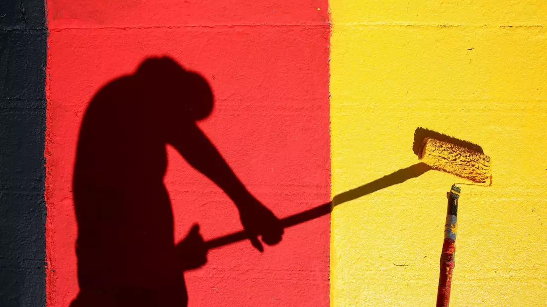 Heute Abend geht es los! Ein Helfer lackiert Kurvensteine in den Farben Schwarz-Rot-Gold. - Bild: Jan Woitas/dpa