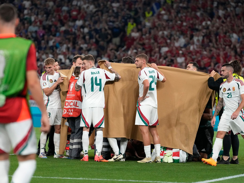 Die ungarischen Spieler halten einen Sichtschutz, während Stürmer Barnabas Varga behandelt wird. - Foto: Antonio Calanni/AP