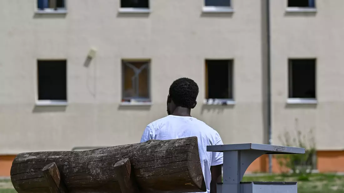 Ein Migrant sitzt auf einer Bank auf dem Gelände der Zentralen Erstaufnahmeeinrichtung für Asylbewerber des Landes Brandenburg in Eisenhüttenstadt. (Archivfoto) - Bild: Patrick Pleul/dpa