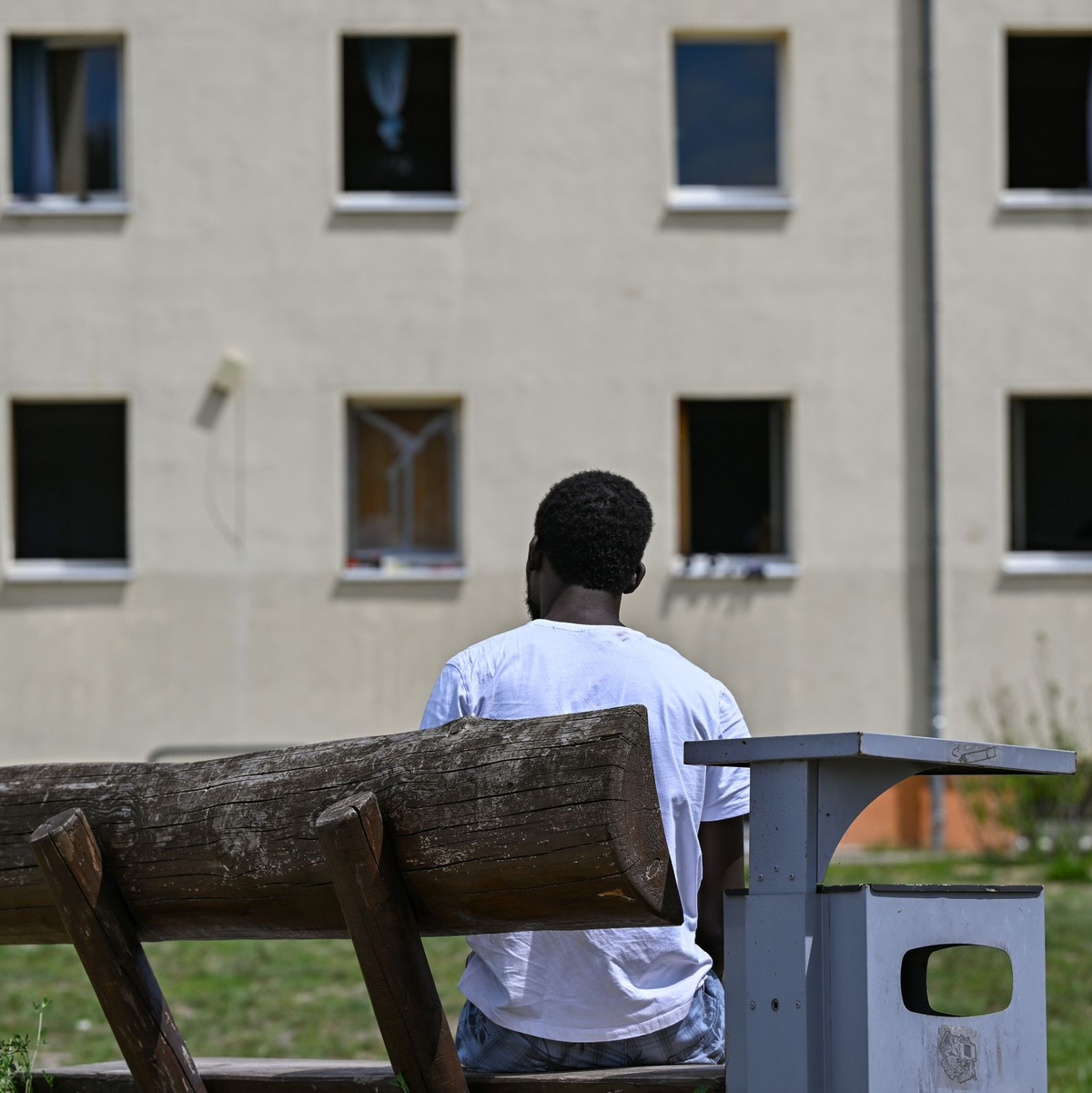 Ein Migrant sitzt auf einer Bank auf dem Gelände der Zentralen Erstaufnahmeeinrichtung für Asylbewerber des Landes Brandenburg in Eisenhüttenstadt. (Archivfoto) - Foto: Patrick Pleul/dpa