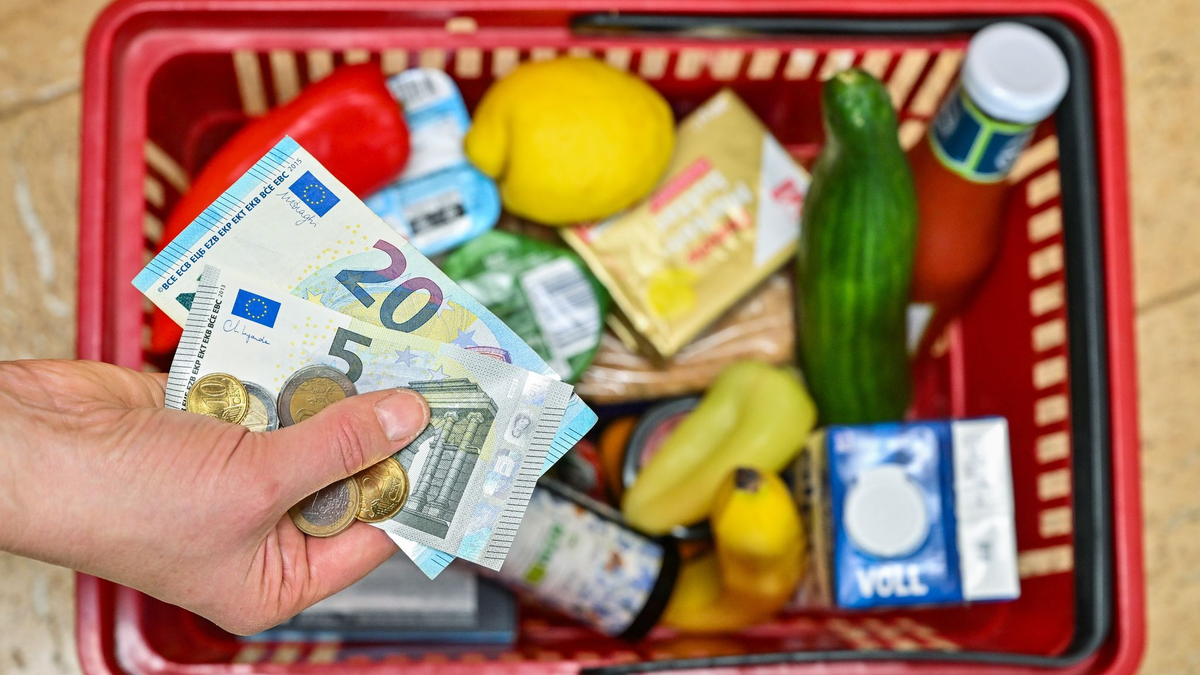 Eine Frau hält auf ihrer Hand Geldscheine vor einem Korb mit Einkäufen - Foto: Patrick Pleul/dpa