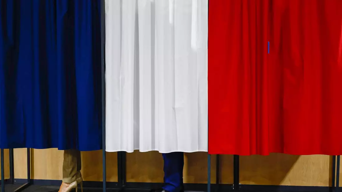 Der französische Präsident Emmanuel Macron und seine Frau Brigitte Macron stehen vor der Stimmabgabe in der Wahlkabine. - Bild: Yara Nardi/Reuters Pool/AP/dpa