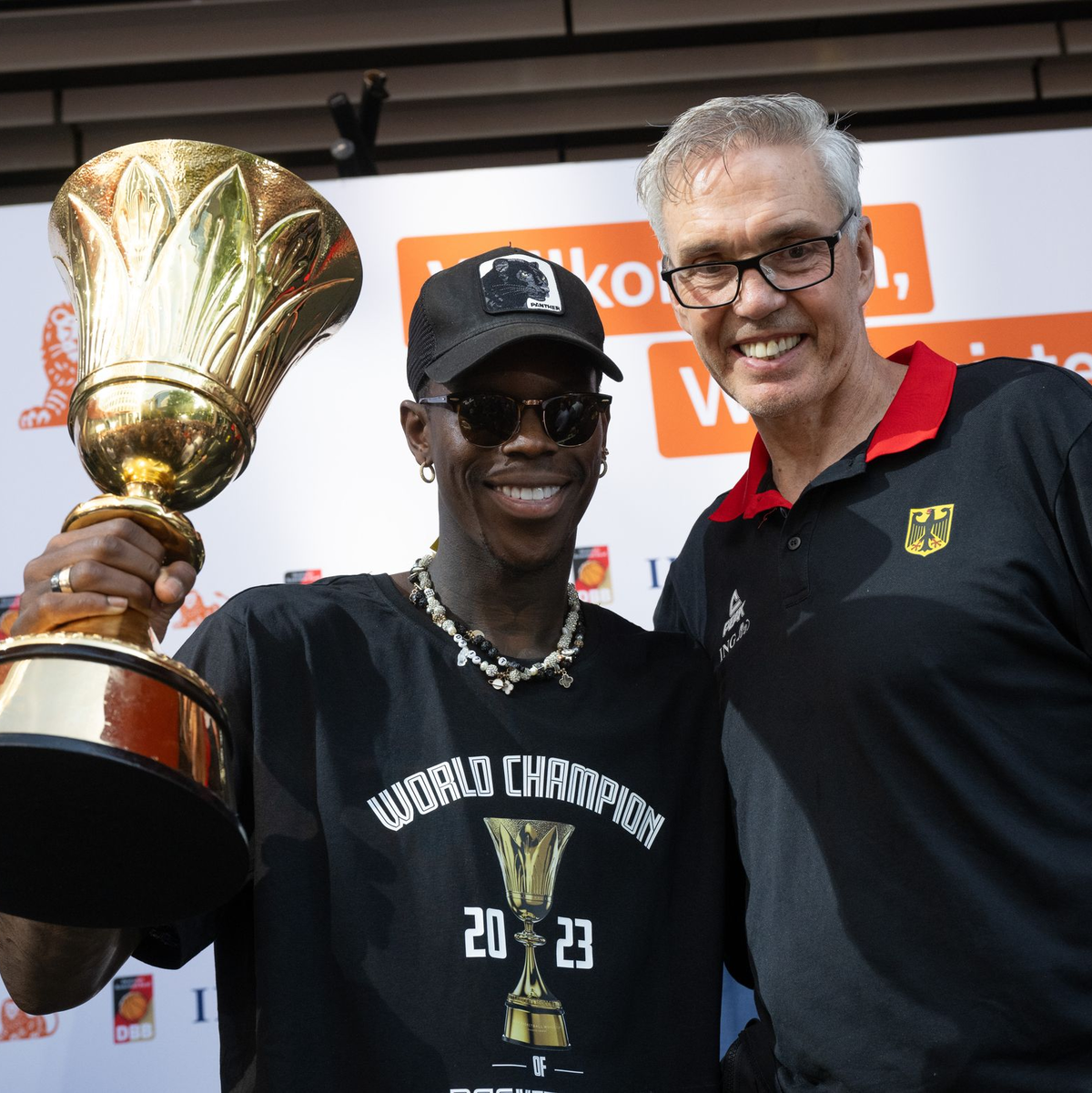 Bundestrainer Gordon Herbert (r) und sein Kapitän Dennis Schröder mit dem WM-Pokal. - Foto: Boris Roessler/dpa