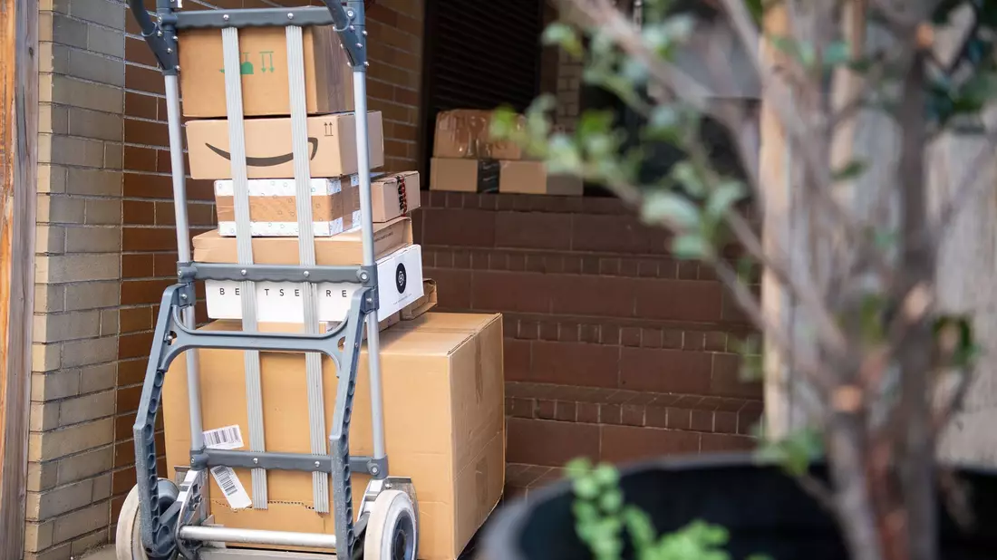Pakete stehen auf einer Karre, während ein Paketzusteller Pakete ausliefert. - Bild: Sebastian Gollnow/dpa