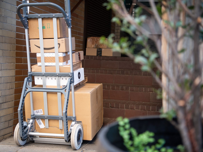 Pakete stehen auf einer Karre, während ein Paketzusteller Pakete ausliefert. - Foto: Sebastian Gollnow/dpa