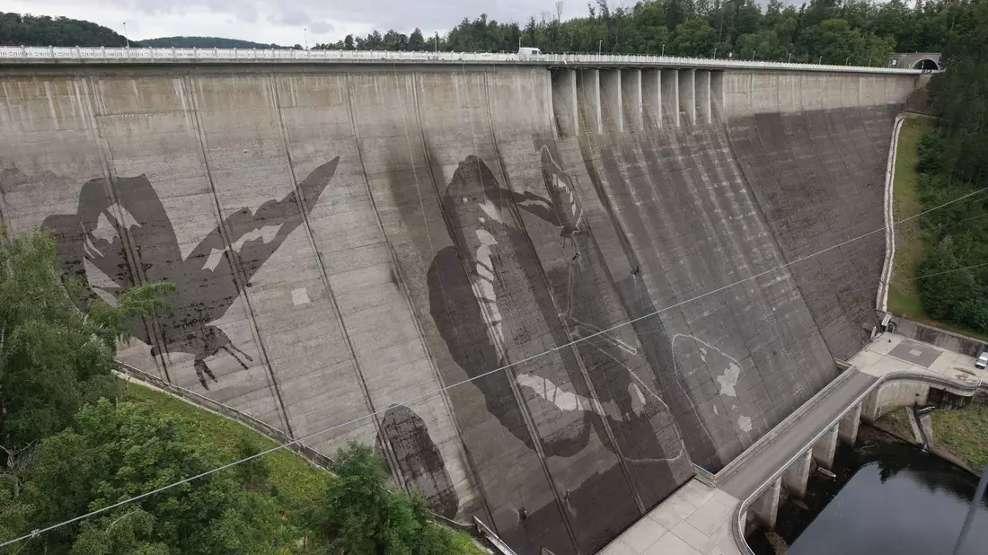 Auf der Staumauer der größten Trinkwassertalsperre Deutschlands wird mit Hochdruckreinigern ein Kunstwerk gemalt.  - Bild: Matthias Bein/dpa