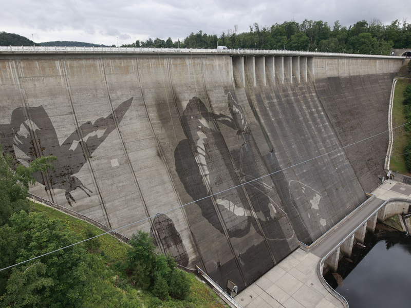Auf der Staumauer der größten Trinkwassertalsperre Deutschlands wird mit Hochdruckreinigern ein Kunstwerk gemalt.  - Foto: Matthias Bein/dpa