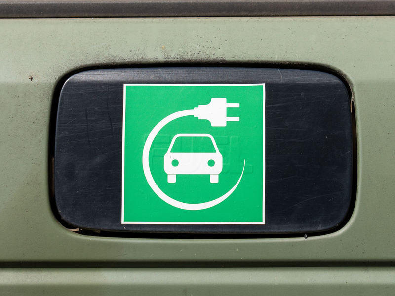 Ein Elektroauto-Symbol auf einem Auto.  - Foto: Soeren Stache/dpa
