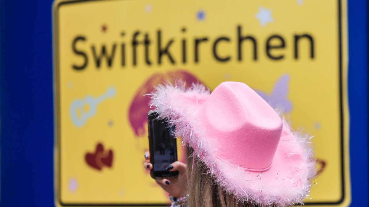 Ein Fan fotografiert vor dem Konzert der Sängerin Taylor Swift in Gelsenkirchen ein «Swiftkirchen»-Schild. Während des Konzerts am Abend zog der Datenverbrauch in den Handynetzen in der Veltins Arena kräftig an. - Foto: Oliver Berg/dpa