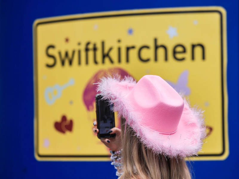 Ein Fan fotografiert vor dem Konzert der Sängerin Taylor Swift in Gelsenkirchen ein «Swiftkirchen»-Schild. Während des Konzerts am Abend zog der Datenverbrauch in den Handynetzen in der Veltins Arena kräftig an. - Foto: Oliver Berg/dpa