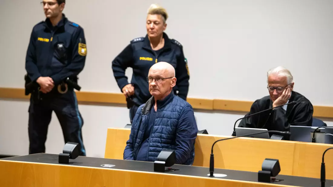 Der wegen der Ermordung von drei Nachbarn angeklagte Mann wird im Gerichtssaal von Polizisten bewacht. Der Mann will nach Angaben seines Anwalts auf Bildern nicht unkenntlich gemacht werden. (Archivfoto) - Bild: Stefan Puchner/dpa