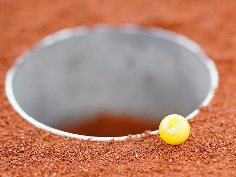 Die Murmeln müssen in das Loch (eine Kuhle) auf dem drei Mal sechs Meter großen Feld befördert werden. - Foto: Uwe Anspach/dpa