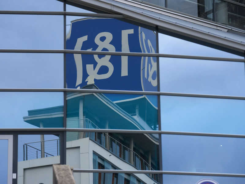 Das 1&1-Firmenlogo auf dem Dach eines Firmengebäudes spiegelt sich in einer Glasfassade. - Foto: Thomas Frey/dpa