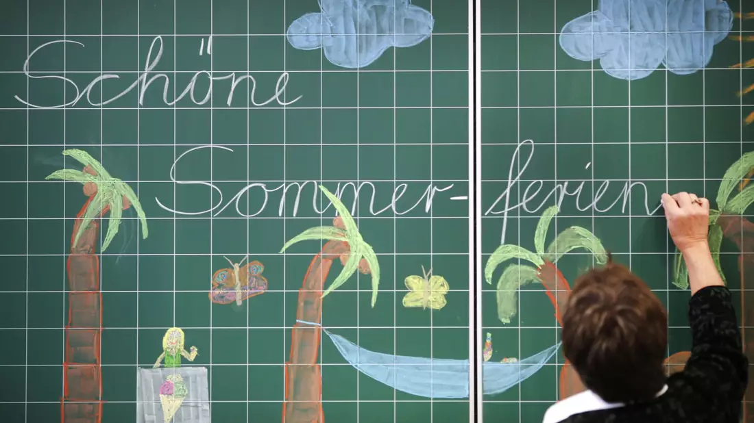 Eine Lehrerin schreibt «Schöne Sommerferien» an die Tafel einer Grundschulklasse. (Archivfoto) - Bild: Ina Fassbender/dpa