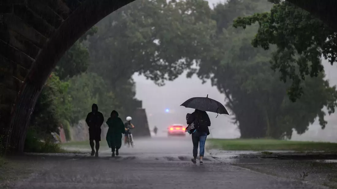 Menschen sind bei starkem Regen in Dresden während eines Gewitters auf dem Elberadweg unterwegs. - Bild: Robert Michael/dpa