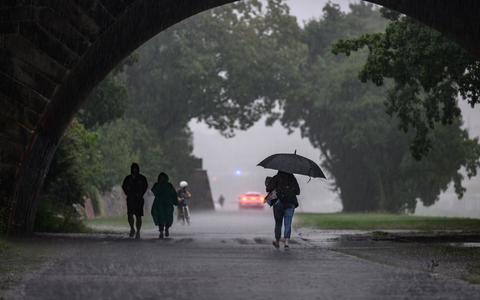 Menschen sind bei starkem Regen in Dresden während eines Gewitters auf dem Elberadweg unterwegs. - Foto: Robert Michael/dpa