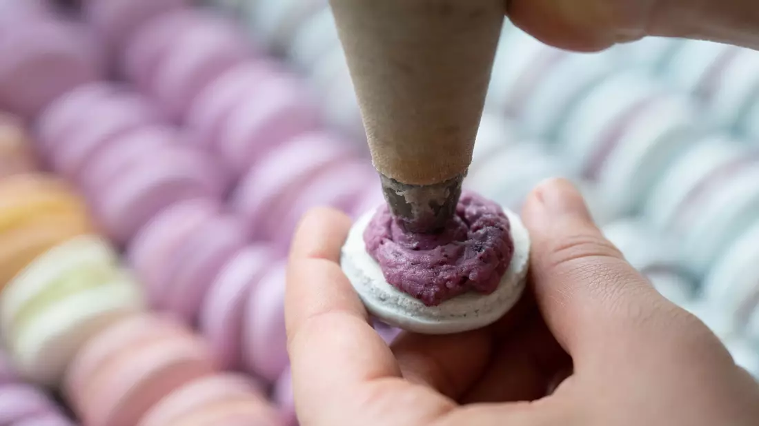 Das Baisergebäck Macaron wird in einer Bäckerei mit einer Spritztüte befüllt. (Archivbild) - Bild: Sebastian Kahnert/dpa