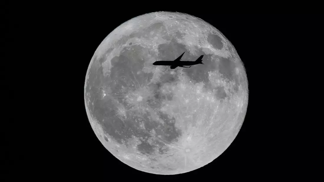 Ein Flugzeug fliegt an einem großen Vollmond vorbei. - Bild: Ringo Chiu/SOPA Images/ZUMA Press Wire/dpa