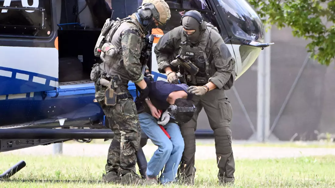 Der Tatverdächtliche wurde in Karlsruhe von bewaffneten Polizisten in Spezialausrüstung vom Helikopter zu einer Wagenkolonne gebracht. - Bild: Uli Deck/dpa