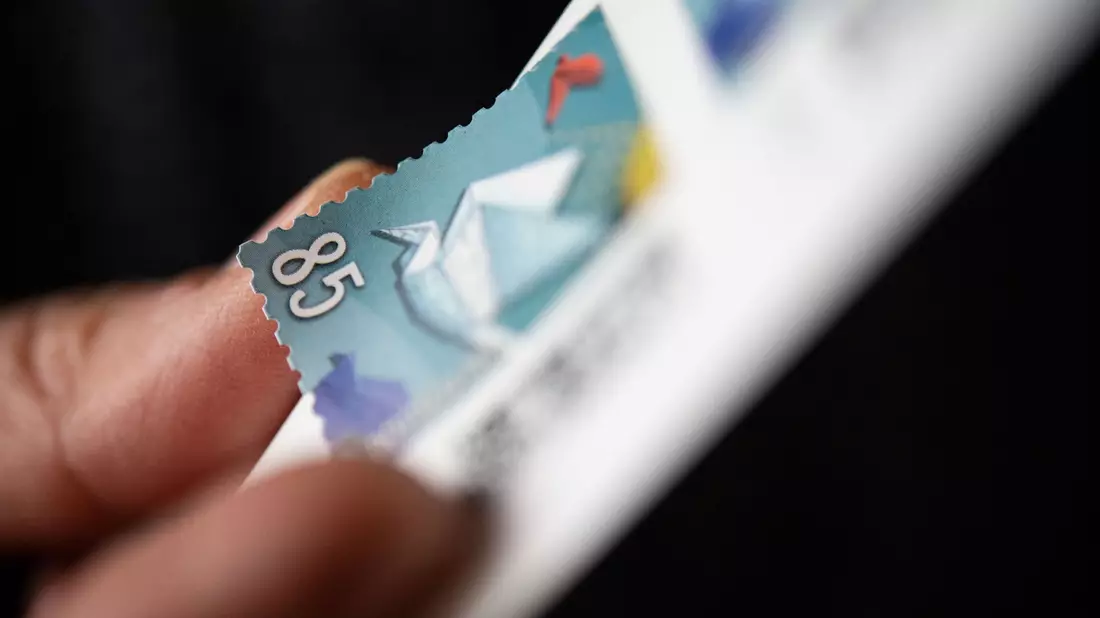 Eine Frau löst eine Briefmarke von einem Briefmarken-Bogen, um sie auf einen Brief zu kleben. - Bild: Marijan Murat/dpa
