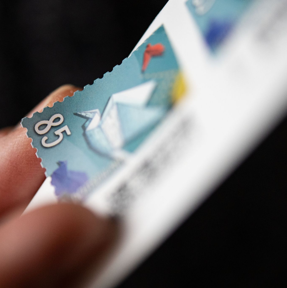 Eine Frau löst eine Briefmarke von einem Briefmarken-Bogen, um sie auf einen Brief zu kleben. - Foto: Marijan Murat/dpa